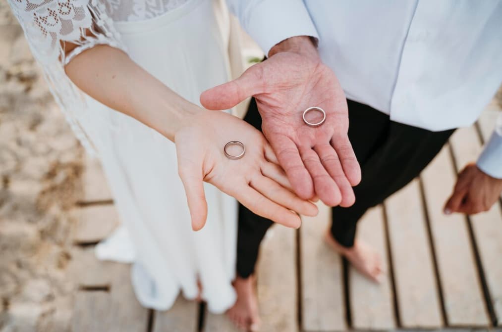 A couple holds hands, showcasing simple silver wedding bands