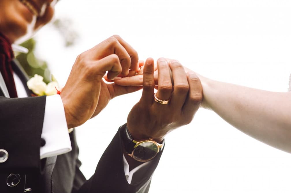 A partner slides a gold band onto the other's finger during a ceremony