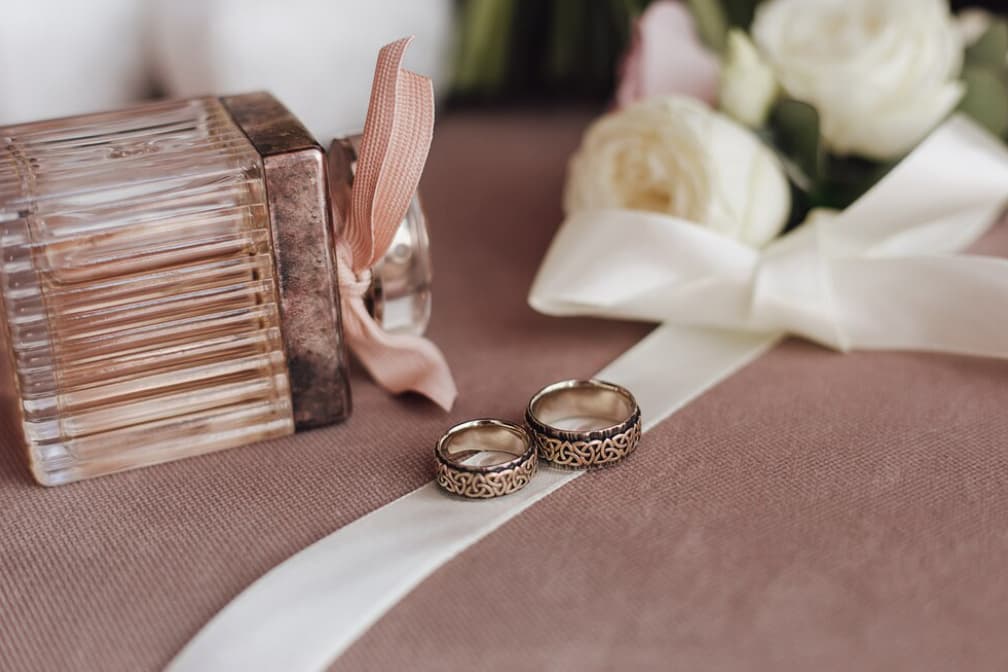 Patterned wedding bands with white ribbon and roses on a satin cloth