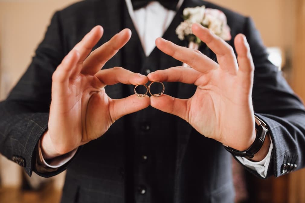 A groom holds two wedding rings in front of his suit