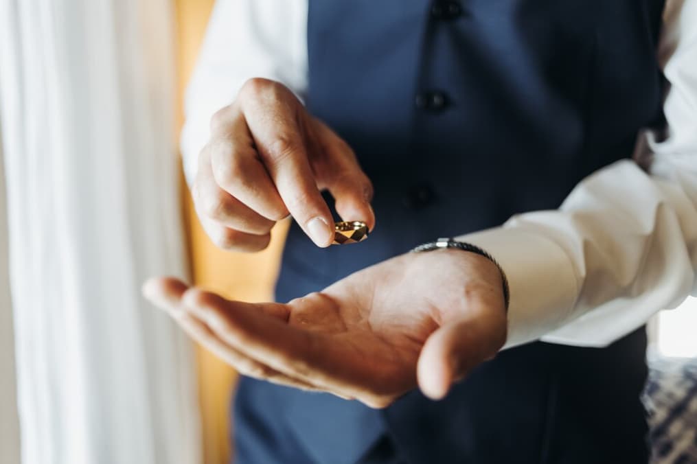 A groom carefully inspects a wedding ring over his palm