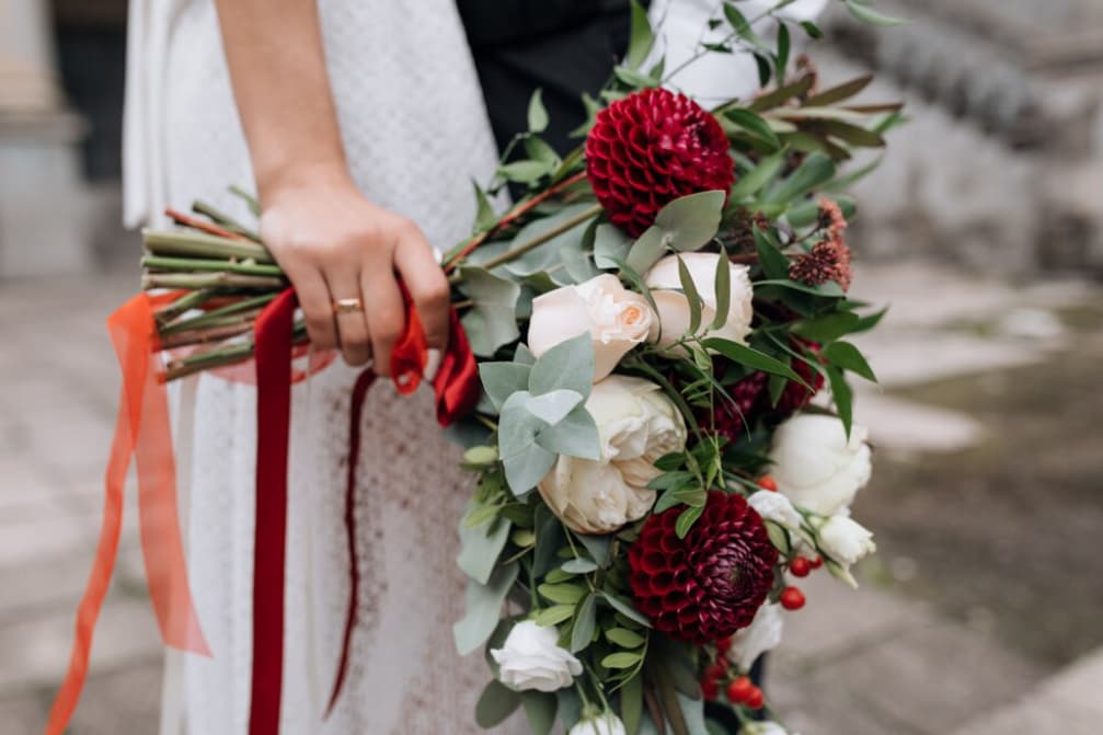 A wedding bouquet with red flowers and trailing ribbons