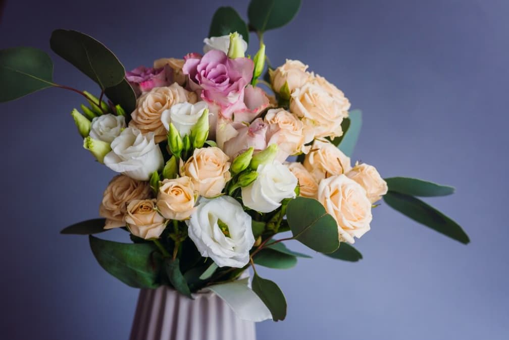  A pastel bouquet of roses and lisianthus in a white vase against a purple backdrop